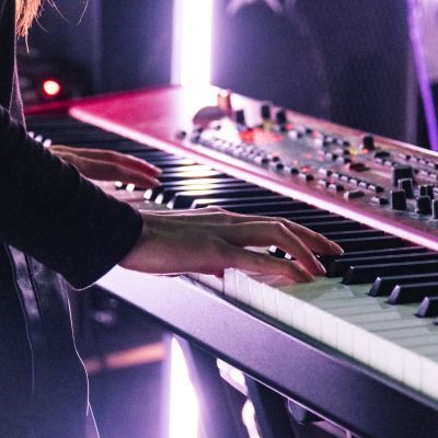 Electronic and Produced Music Students playing the keyboard on stage with a pink hue light in the background
